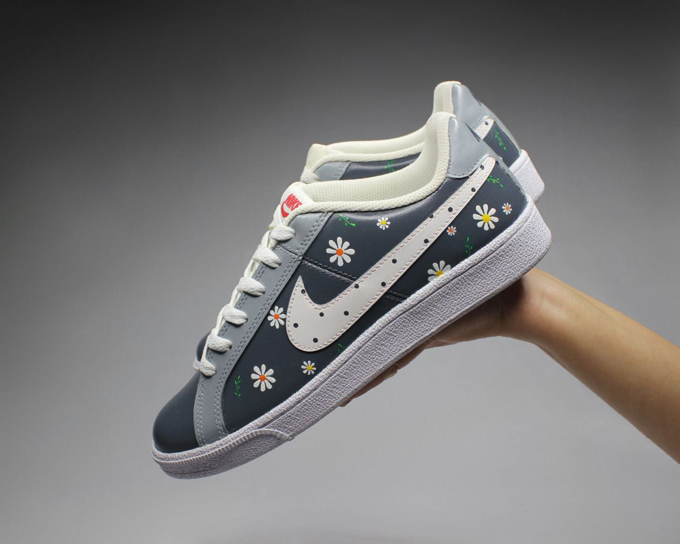 Hand-painted grey sneaker with white, orange, yellow floral patterns on grey background where sneakers are held by hand