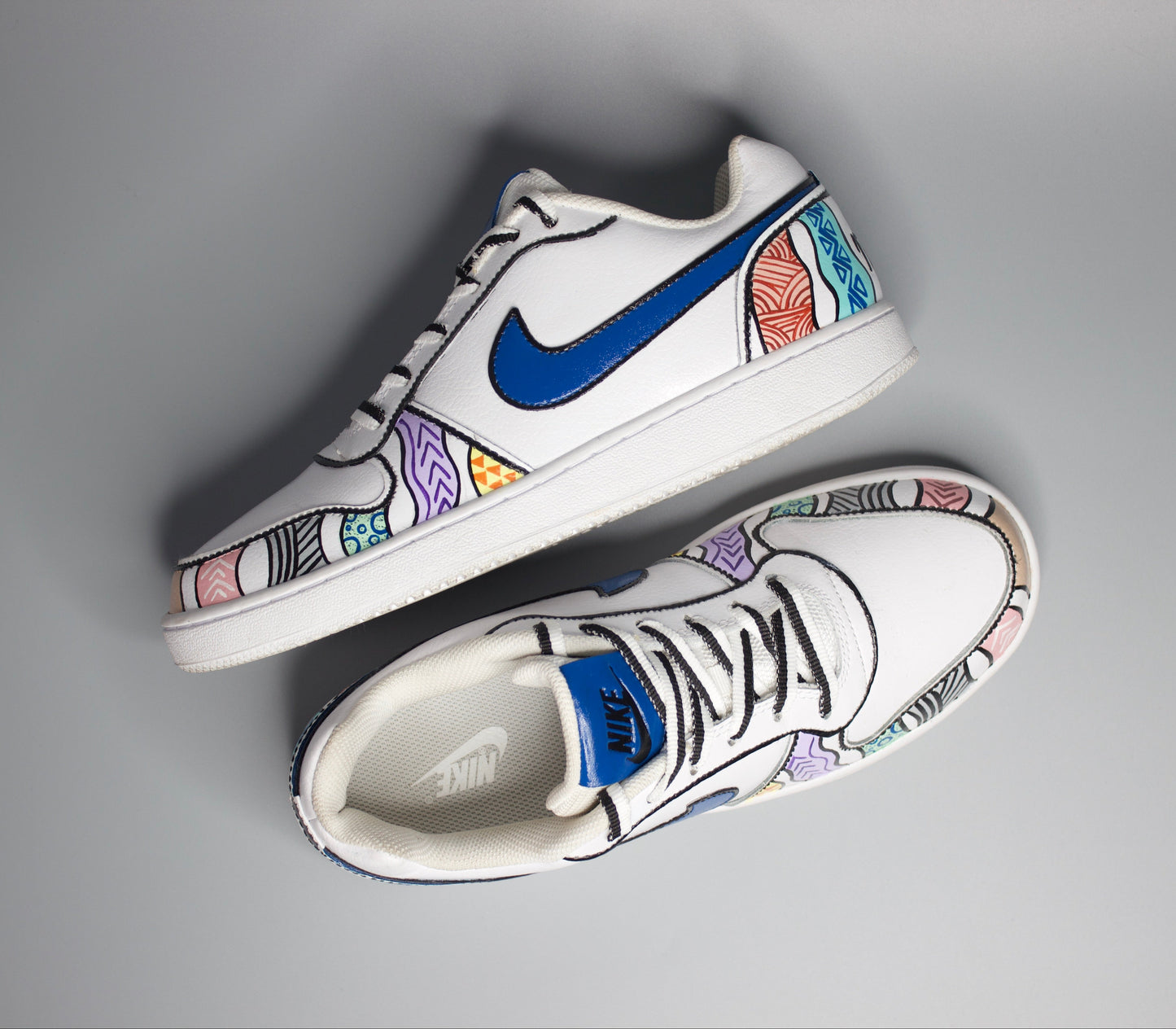 Hand-painted sneakers with colorful patterns and motifs and blue swoosh logo on a gray background