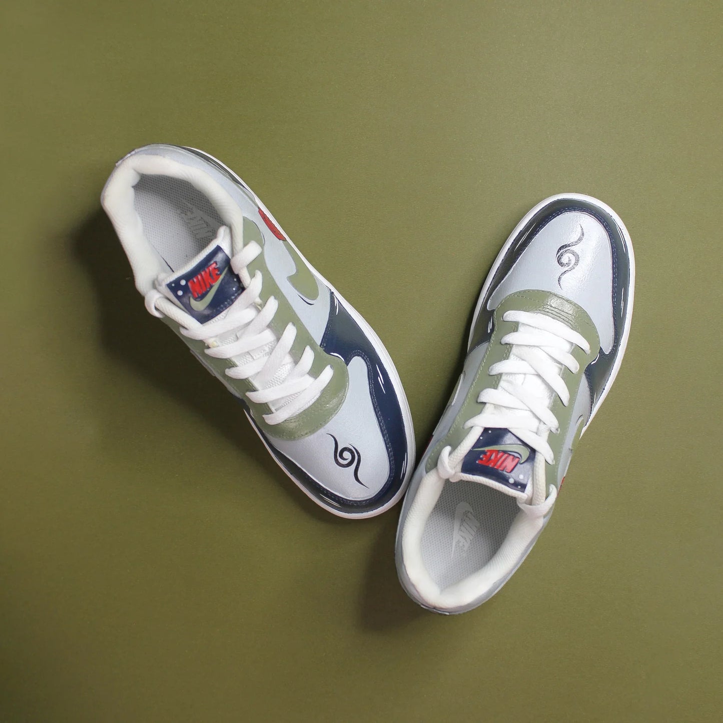 A hand-painted Pair of white Nike sneakers with blue, green and grey accents on a green background. a unique design inspired by the Naruto universe.