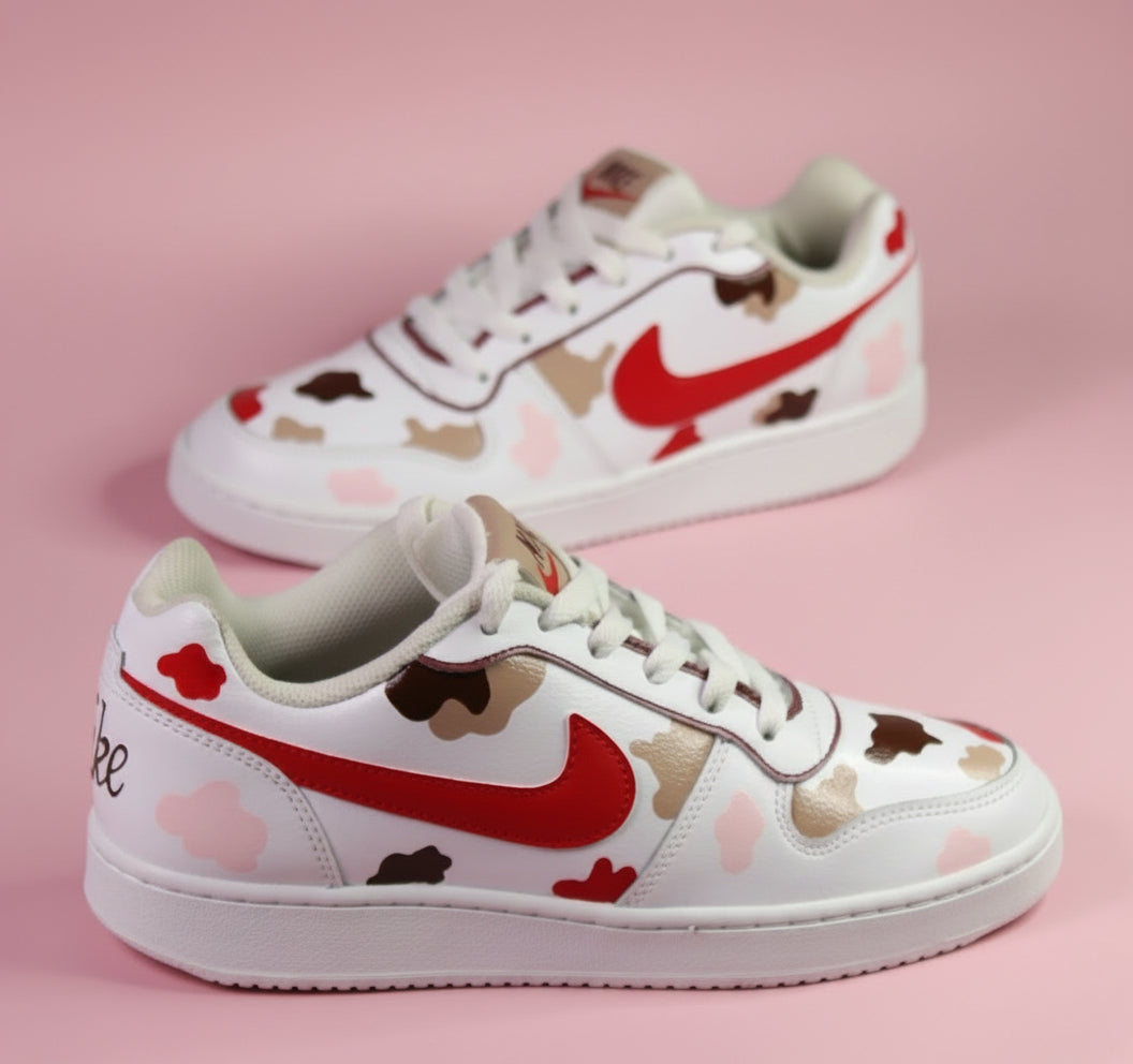 White Nike sneakers with red swoosh logo and colourful camouflage designs with beige, brown and pink on a pink background