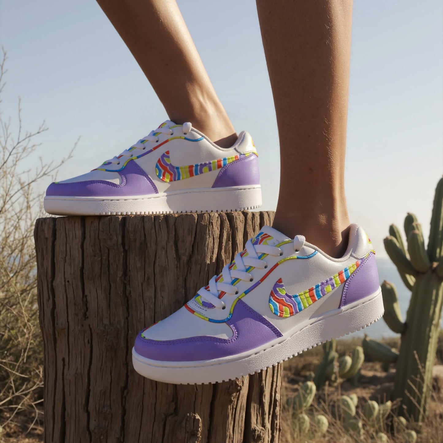 Purple and white sneakers with rainbow accents on a wooden stump against a desert background
